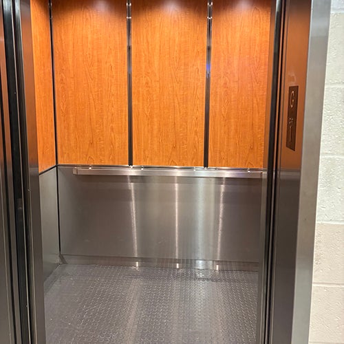 inside of a clean, modern elevator with stainless steel walls and a wood-paneled back wall.