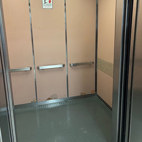 beige-paneled elevator interior with two metal handrails and a fire safety sign.