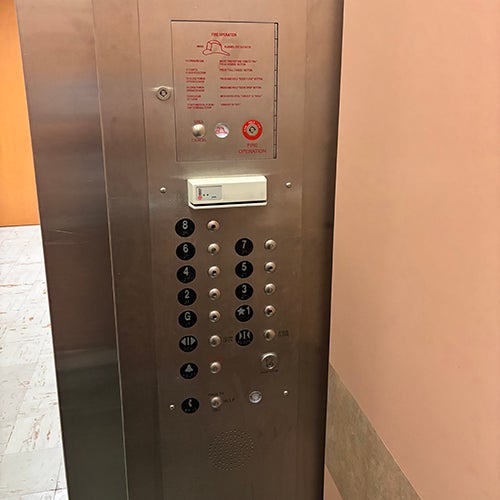 control panel for an elevator with buttons for each floor with some visible scuffing at the bottom.