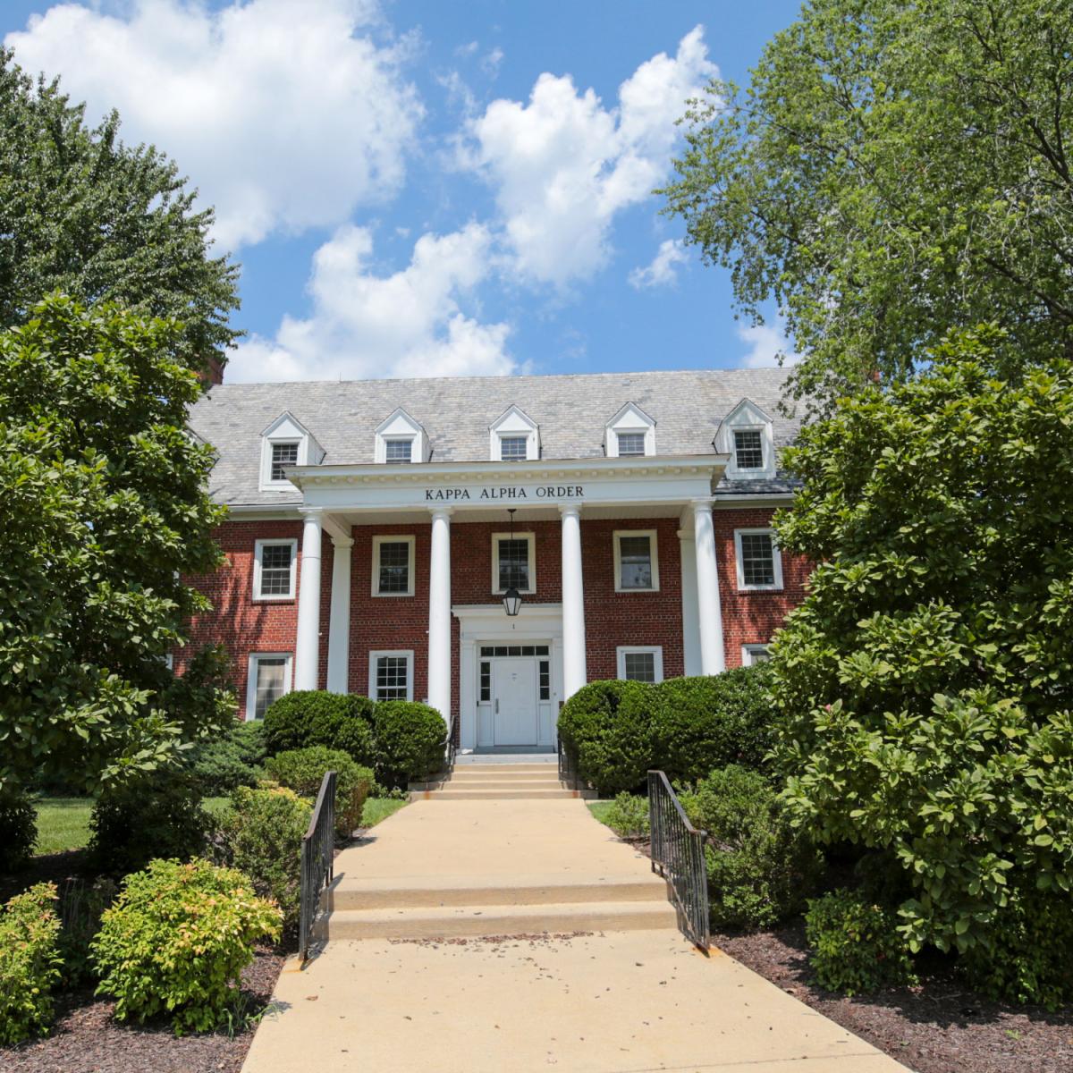 Brick house at 1 Fraternity Row with white columns and surrounding greenery