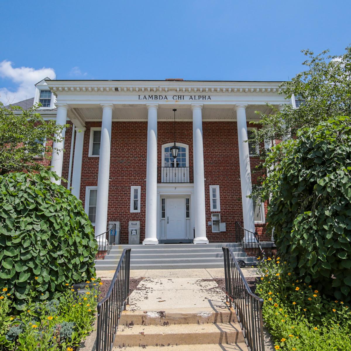 Brick house at 7 Fraternity Row with white columns and surrounding greenery