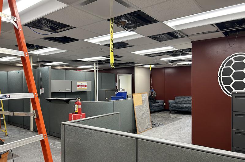 Annapolis Hall office during HVAC renovations, featuring open ceiling tiles, yellow caution tape, and an orange ladder.