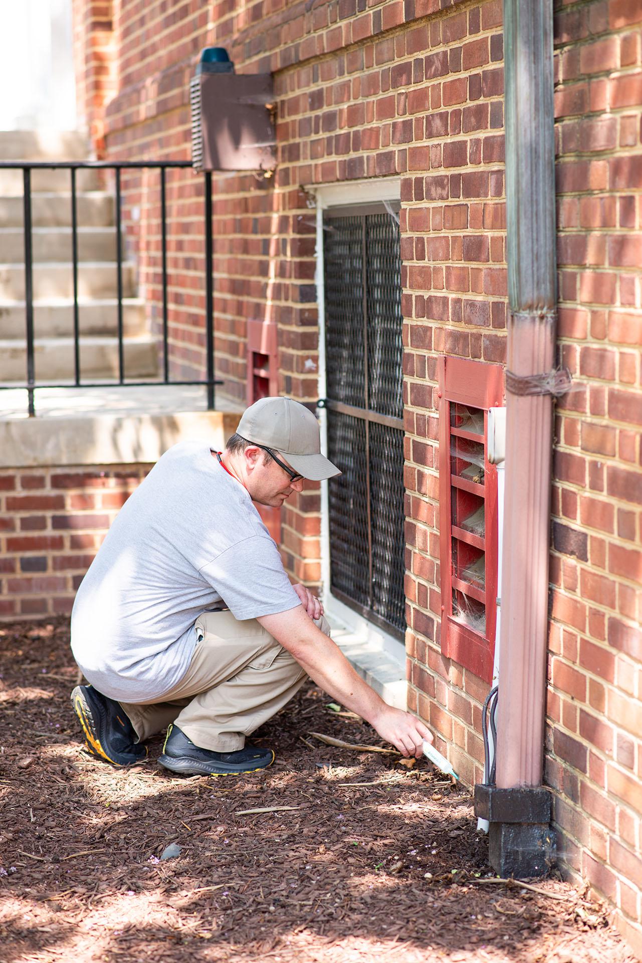 DRF staff applying ant gel insecticide to the exterior brick wall of a residence hall