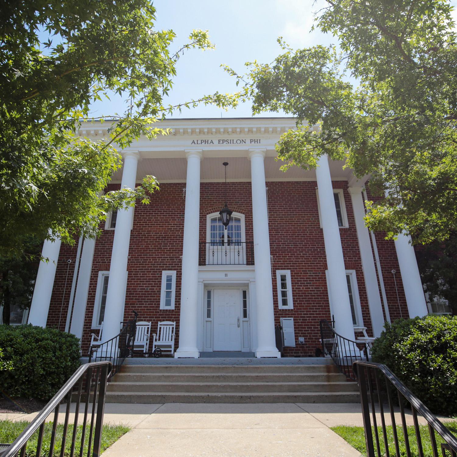 Brick house at 11 Fraternity Row with white columns and surrounding greenery