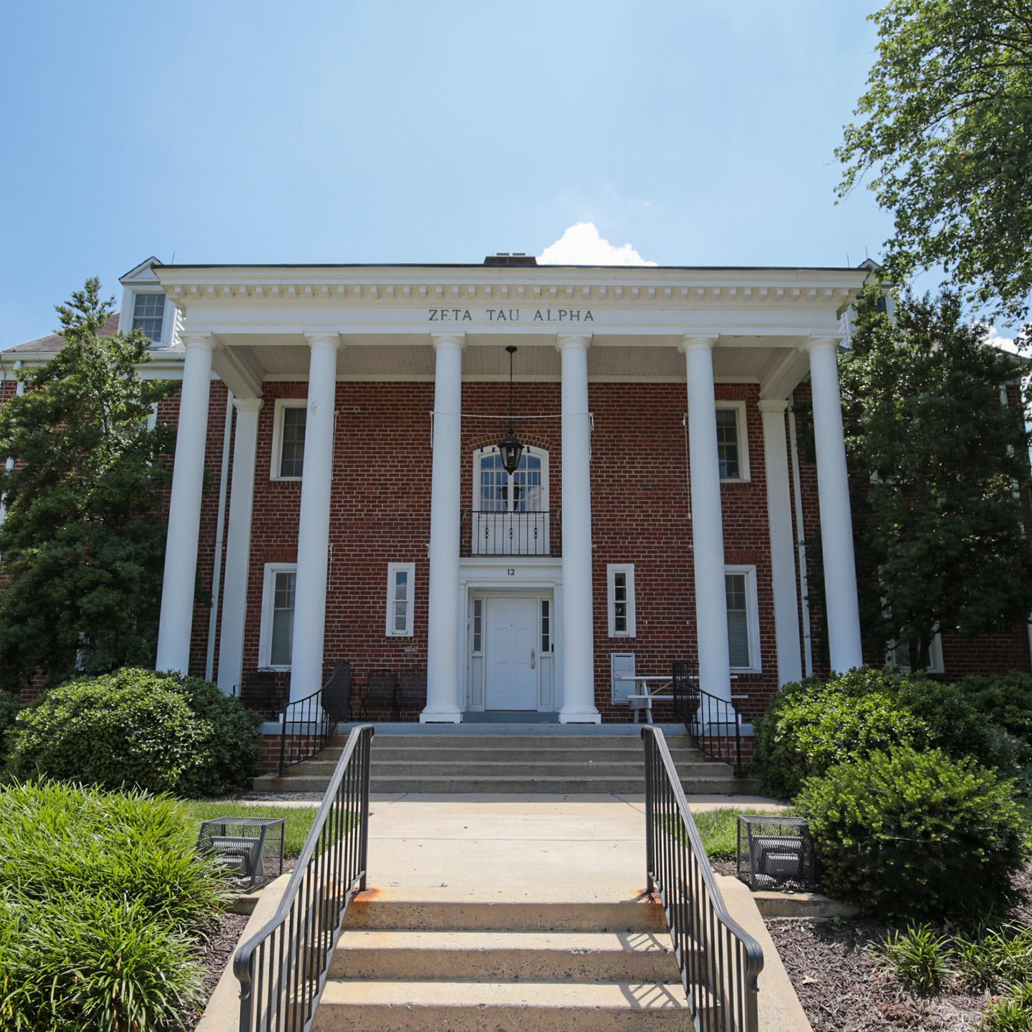 Brick house at 12 Fraternity Row with white columns and surrounding greenery
