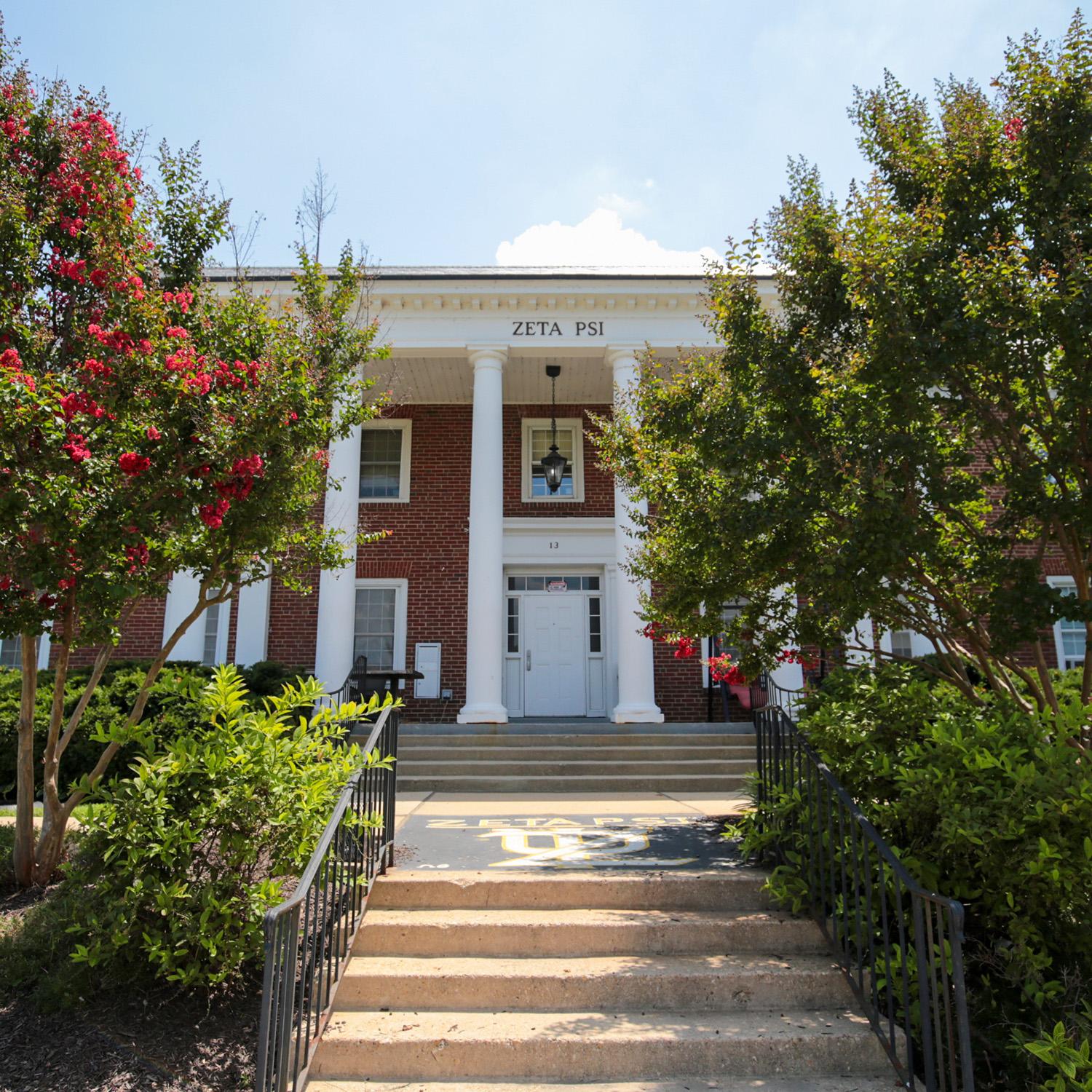 Brick house at 13 Fraternity Row with white columns and surrounding greenery
