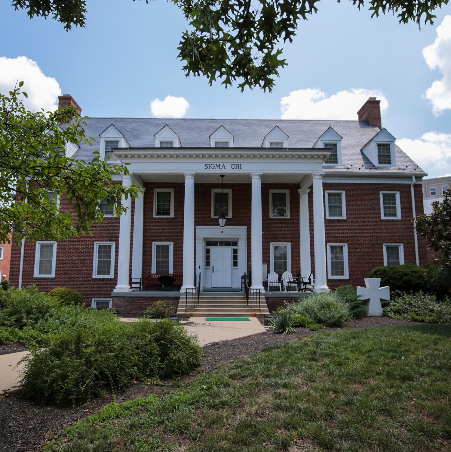 Brick house at 14 Fraternity Row with white columns and surrounding greenery