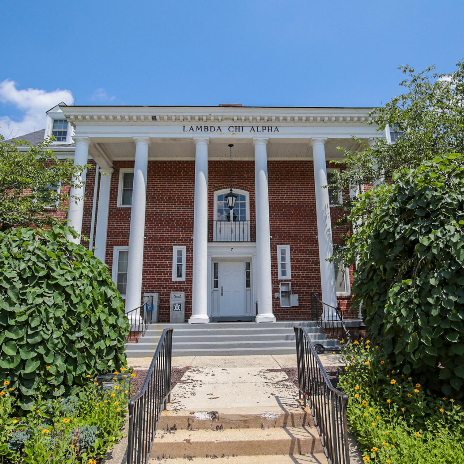 Brick house at 7 Fraternity Row with white columns and surrounding greenery