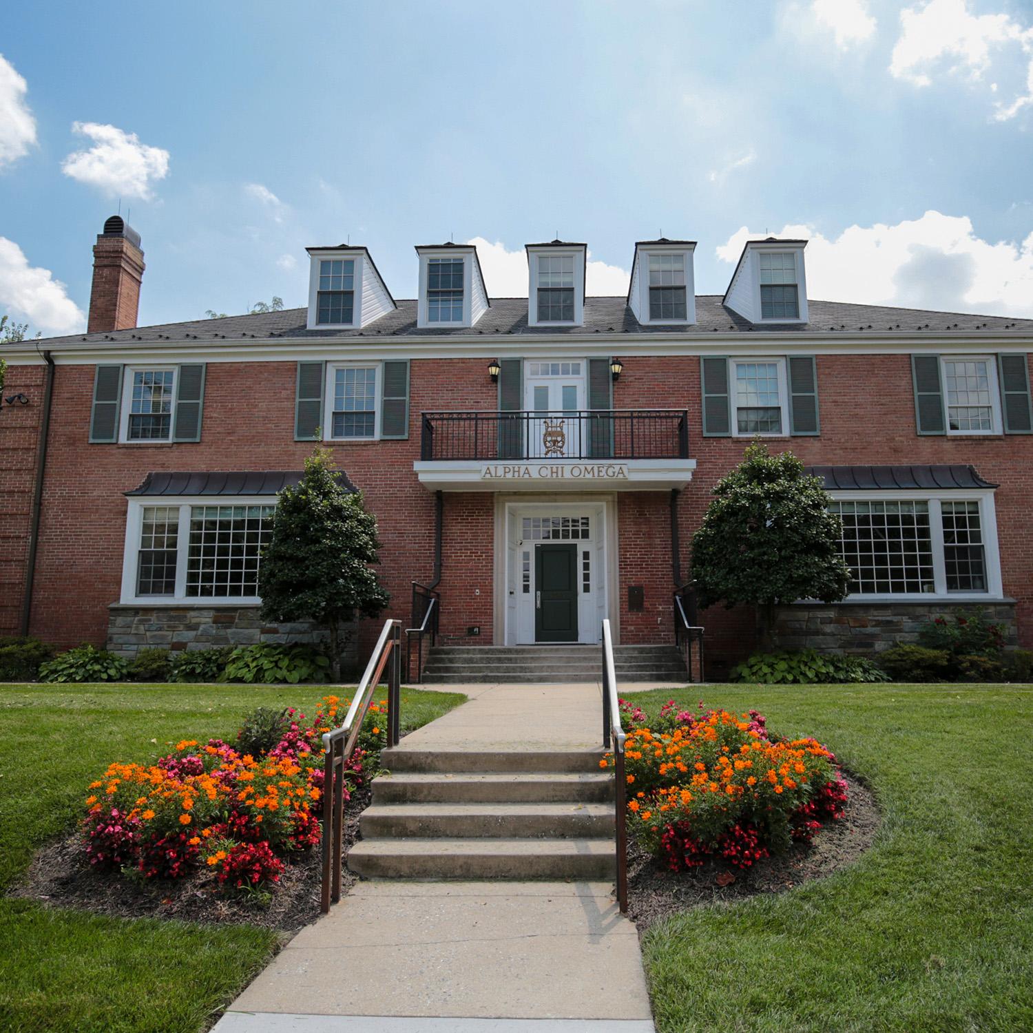 Brick house at 4525 College Avenue with window shutters, white columns, and a front entrance framed by colorful flower beds.