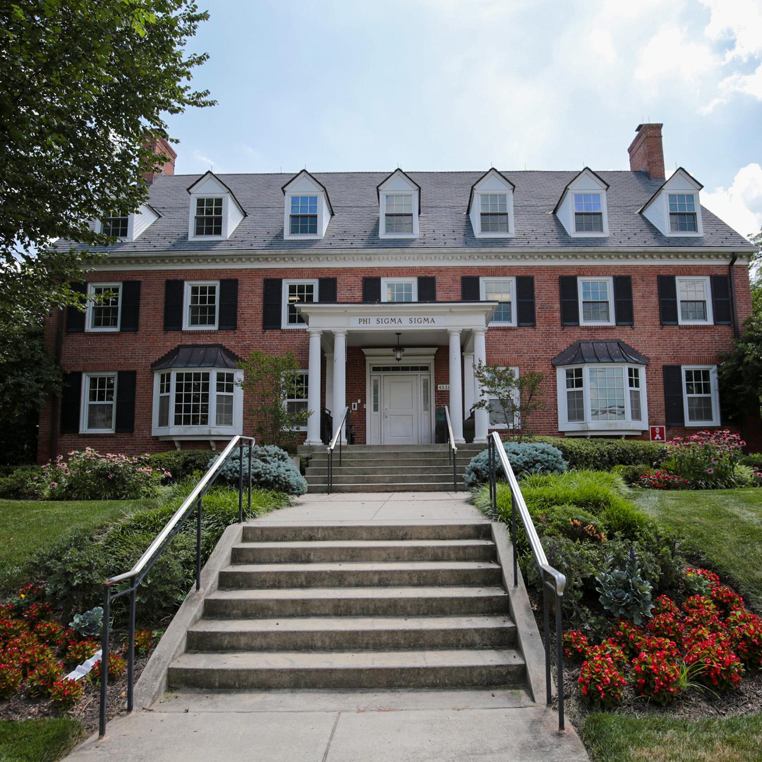Brick house at 4531 College Avenue with window shutters, white columns, and a front entrance framed by surrounding greenery