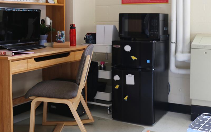 Residence hall room with wooden desk, chair, and microfridge.