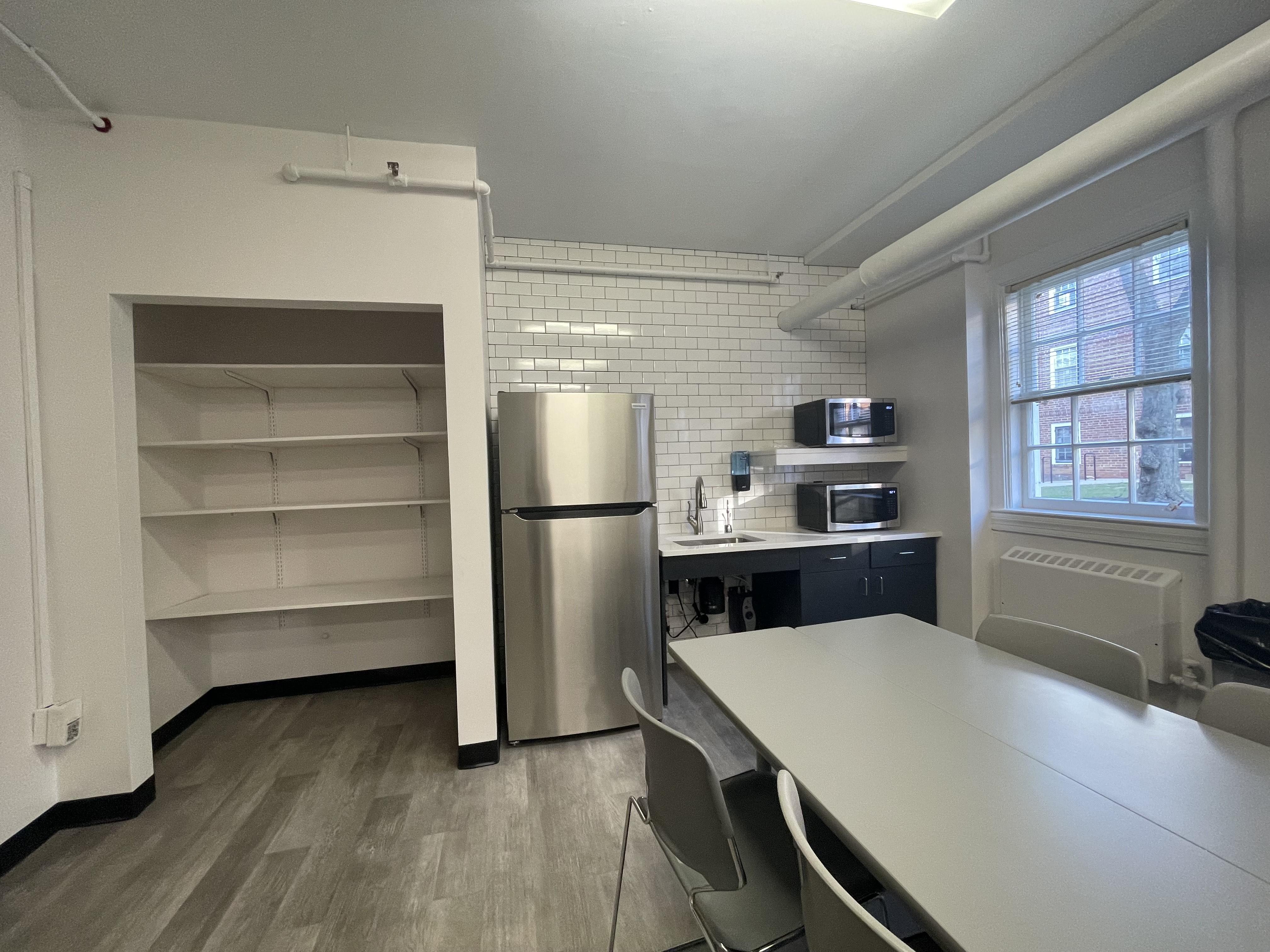 Break room with table seating, kitchenette area, refrigerator, microwave and open shelving in the renovated ground floor of Caroline Hall.