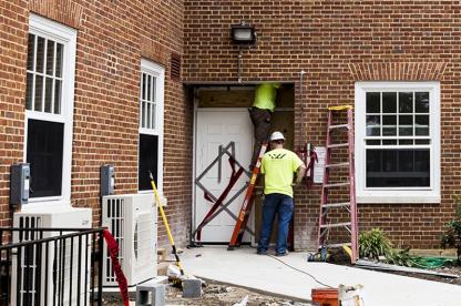 Two facilities workers in neon shirts repairing an exterior doorway of Dorchester Hall.